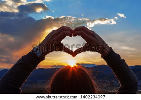 woman silhouette at sunset or dawn, hands form a heart shape