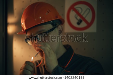 worker smokes near the sign no smoking