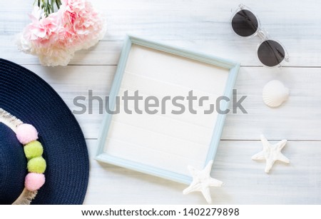 top view of summer blue female hat and picture frame with sunglasses and seashell and star fish decoration on white wood table.summer vacation