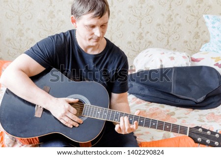 pictured in the photo a man sits and plays the guitar