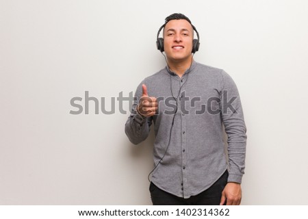 Young latin man listening to music smiling and raising thumb up