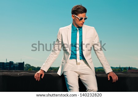 Retro fifties summer fashion man with white suit and sunglasses. On rooftop. Blue sky. Royalty-Free Stock Photo #140232820