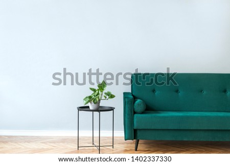 Minimalistic and luxury grey home interior with green  velvet design sofa, black coffe table with plant . Copy space for inscription, mock up poster. Brown wooden parquet. Grey background walls.