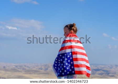 American flag. Back view little patriotic happy girl holding an american flag waving on blue sky background. National 4 july. Memorial day