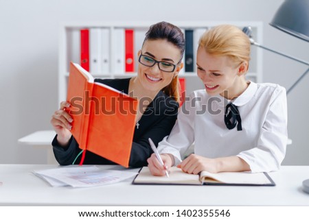 Portrait of gorgeous women working in modern office. Smiling brunette showing something to cheerful blonde. Ladies talking and laughing. Workflow in full swing. Blurred background
