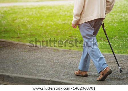elderly old man with walking stick stand on footpath sidewalk crossing the street alone roadside in public park. concept senior across the street. soft focus Royalty-Free Stock Photo #1402360901