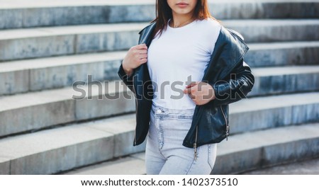 Girl wearing t-shirt with place for logo, glasses and leather jacket posing against street