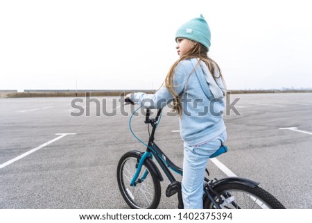 A girl in a hat and a blue sweater on a bicycle stopped and looks around.
