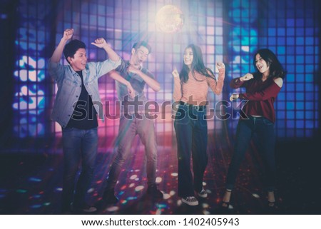 Picture of happy young people dancing together under colorful disco lights in the nightclub