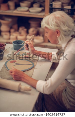 Beautiful picture. Nice aged woman sitting at the table while painting a beautiful flower