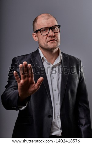 Unhappy busuness man in black suit and glasses showing the palm the stop sign on grey background. Closeup portrait