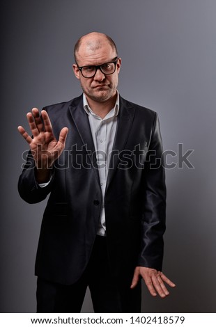 Unhappy busuness man in black suit and glasses showing the palm the stop sign on grey background. Closeup portrait