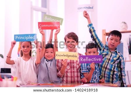 Expressing yourself. Smiling children holding up colorful sheets of paper with English words describing their personalities. Royalty-Free Stock Photo #1402418918