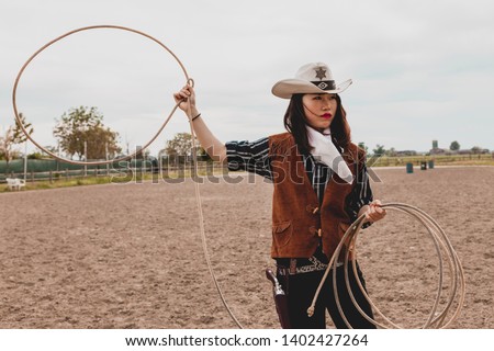 pretty Chinese cowgirl throwing the lasso in a horse paddock on a wild west farm