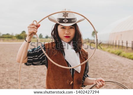 pretty Chinese cowgirl throwing the lasso in a horse paddock on a wild west farm