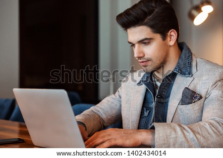Image of a handsome young business man posing indoors in office using laptop computer.