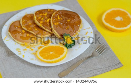 Pancakes with orange for breakfast.
A pile of pancakes on a plate with honey and orange on a bright yellow background. View from above. Food flat