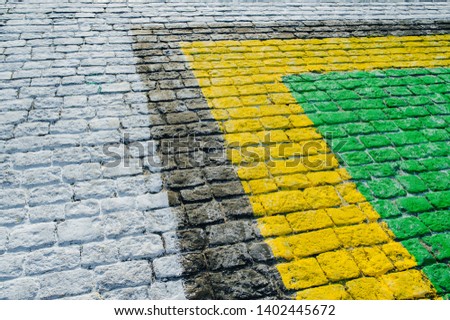 Close-up road paving slabs by mosaic construction. Yellow, green, black, white paving cobbles. Corner in color.