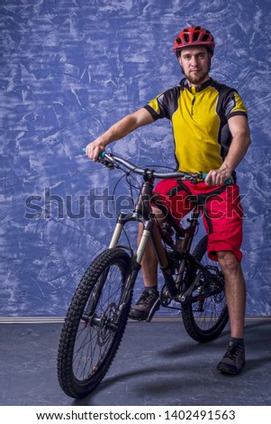 Cyclist in a yellow T-shirt and red shorts is sitting on a mountain bike against the background of a blue wall. Full suspension. Active lifestyle, cycling.