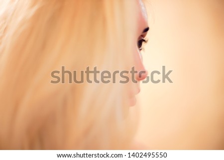 Soft image in profile of a girl with lush long blond hair. Selective focus on the eye with natural long eyelashes. Warm light.