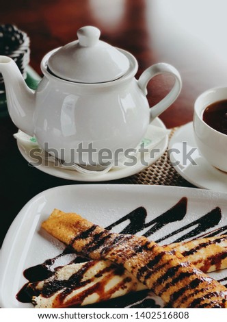 Beautiful breakfast, pancakes with chocolate and powdered sugar.  Breakfast on the terrace in white dishes. Tea in a teapot and a mug of hot tea.