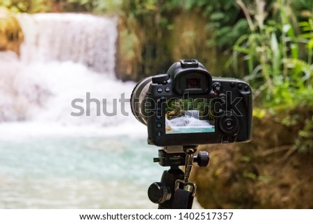 Professional camera photographing on a long exposure of a beautiful waterfall Kuang si in Laos. SLR camera on a tripod shooting a video of the water fall. Wildlife photography.