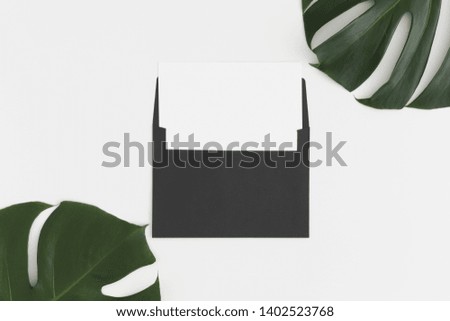 Top view of a white card mockup with monstera leaf decoration on a white table.