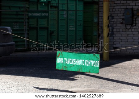 Green old rusty customs area sign at entrance to customs clearance with the inscription in Russian with freight railcar at background. Russian translation: Customs control zone.