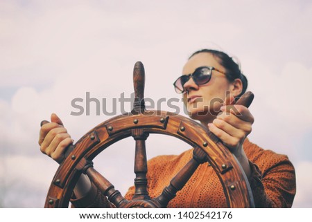 The girl controls the yacht, hands on the steering wheel,  handwheel on sky background