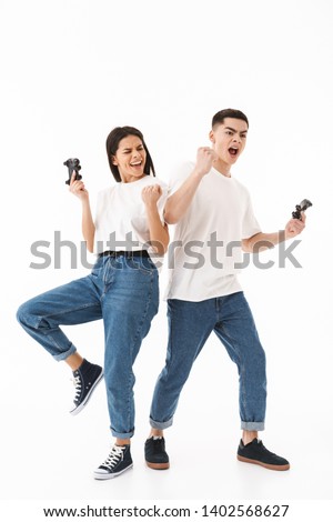 Full length portrait of a young attractive couple standing isolated over white background, playing video games, celebrating