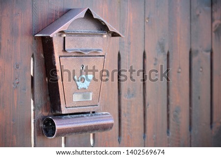 Brown textured metal postbox with a mail horn icon hanging on a wooden fence. Concept of mailbox and post delivery with copy space.