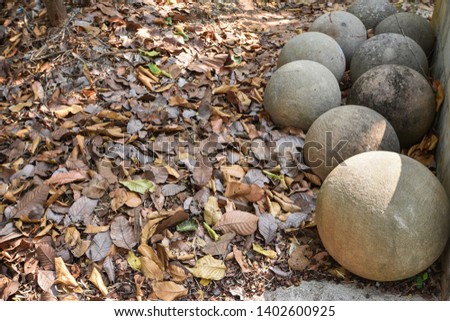 Stone balls or rock balls on the ground in the wild filled grey and brown tree leaves in the nature; the balls are carved by man to use as house garden decoration objects or to use in Buddhist temple