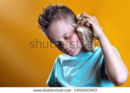 a boy in a light t-shirt listens to the sea in a sea shell on a bright colored background