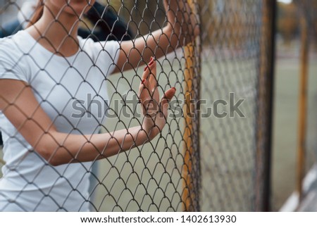 Women in white shirt standing near the fence outdoors at daytime.
