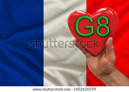 man's hand holds a red heart, on which g 8 is written - a symbol of the international meeting, the G8 summit against the background of the flag of France