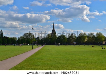 The beautiful typical UK scenery. Green grass and trees in the park on a sunny day with blue sky and fluffy clouds.