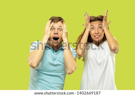 Beautiful young couple's half-length portrait isolated on green studio background. Woman and man are astonished and shocked of the brilliant news. Facial expression, human emotions concept.