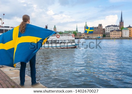 Stockholm, Sweden. National Day of Sweden. Swedish Flag Day. Young man with Swedish Flag on Old Town of Stockholm background. Riddarholmen - part of the historical Old Town, Gamla Stan.