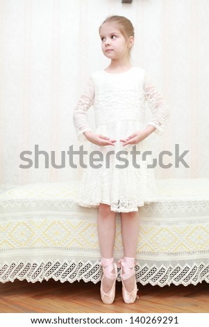 Pretty ballerina in pointe shoes and a white dress standing in a ballet pose against a white curtain