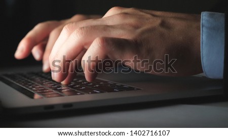 Close up hands of businessman typing text on laptop keyboard at desk in office. Male arms of manager working on notebook late at night. Young entrepreneur using computer on table. Low angle view