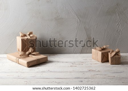holiday gifts wrapped in brown paper against grey background and wooden floor