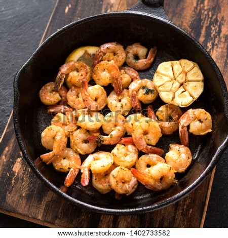 Roasted shrimps with lemon, garlic and herbs. Seafood, shelfish. Shrimps Prawns grilled with spices, garlic and lemon on black stone background, copy space. Shrimps prawns on cast iron pan. 
