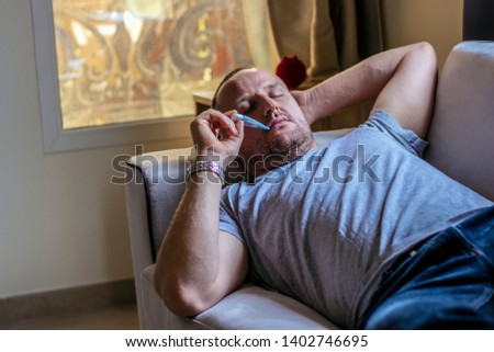 Sick young man laying down in the bed with a thermometer. The concept of medical care to patients at home by yourself.  