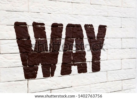 The word" way " is written in brown English letters on a white brick wall. Direction indicator.