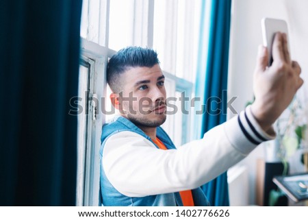 A Smiling Handsome Young Man Taking Self Picture Using Mobile Phone Inside the House.