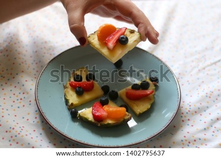 Various spring fruit on a turquoise plate: strawberries, pineapple, blueberries and tangerine. Unrecognizable person reaching for fruit. Selective focus.