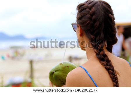 
Girl in braids taking coconut water on the beach, watching the sea