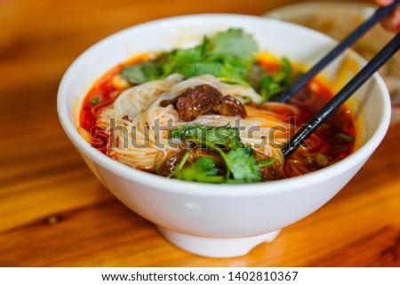 Eating a big bowl of Sichuan spicy rice noodle with beef stew on a wooden table