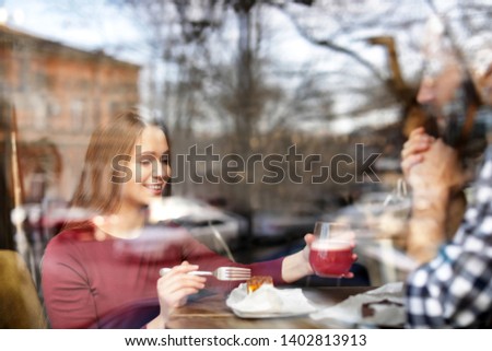 Lovely young couple spending time together in cafe, view from outdoors through window