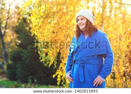 Beautiful autumn woman outdoors. Woman fashion. Young woman dressed in blue coat and warm hat, walking in autumn park. Beautiful girl on fall nature background. People, lifestyle and autumn concept